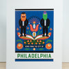 An art print featuring a colorful graphic illustration with two stylized Philadelphia mascots, flowers, and the text 'PHILADELPHIA' and 'ICONS FROM THE CITY OF', shown standing against a light wall on a wood surface.