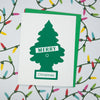 A white greeting card with a green Christmas tree silhouette and the words 'MERRY Christmas' in white, placed on top of a green envelope against a light background with colorful string lights.