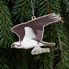 An ornament shaped like an osprey, hanging from a silver string against a background of green pine needles.