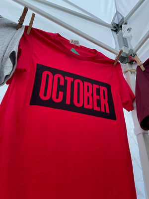 Red t-shirt with 'OCTOBER' printed on it hanging on a rack.