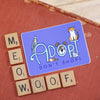 Sticker with 'ADOPT DON'T SHOP!' text and animal illustrations on a red surface with Scrabble tiles.