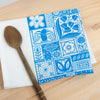 Blue patterned cloth napkin with white designs on a wooden surface next to a wooden spoon.