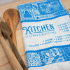 Kitchen towel with 'Kitchen Conversions' text and patterns on a wooden surface with wooden spoons.