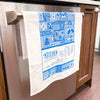 White towel with blue patterns and text hanging on a kitchen appliance handle.