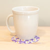 White mug on a purple coaster with a pattern on a wooden surface
