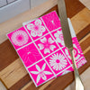 Pink and white floral patterned cutting board with a gold knife on a wooden surface.