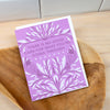 Purple card with white text and bird designs on a wooden surface