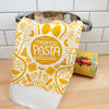 White towel with yellow pasta-themed design and 'more pasta please' text on a kitchen counter.