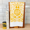 Decorative kitchen towel with 'More Pasta Please' design, book, and jar on a countertop.