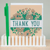 Card with floral design and 'Thank You' text, held by a green pen on a white stand.