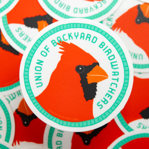 Sticker with a cardinal design and 'Union of Backyard Birdwatchers' text on an orange background.